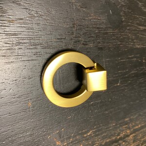 May include: A gold-toned ring pull cabinet knob with a square accent.