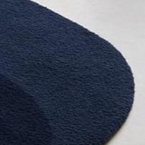Puede incluir: Primer plano de un calcet&iacute;n azul marino con un aspecto suave y texturizado. El calcet&iacute;n est&aacute; hecho de un material afelpado y tiene una punta redondeada. El fondo es de color claro y neutro.