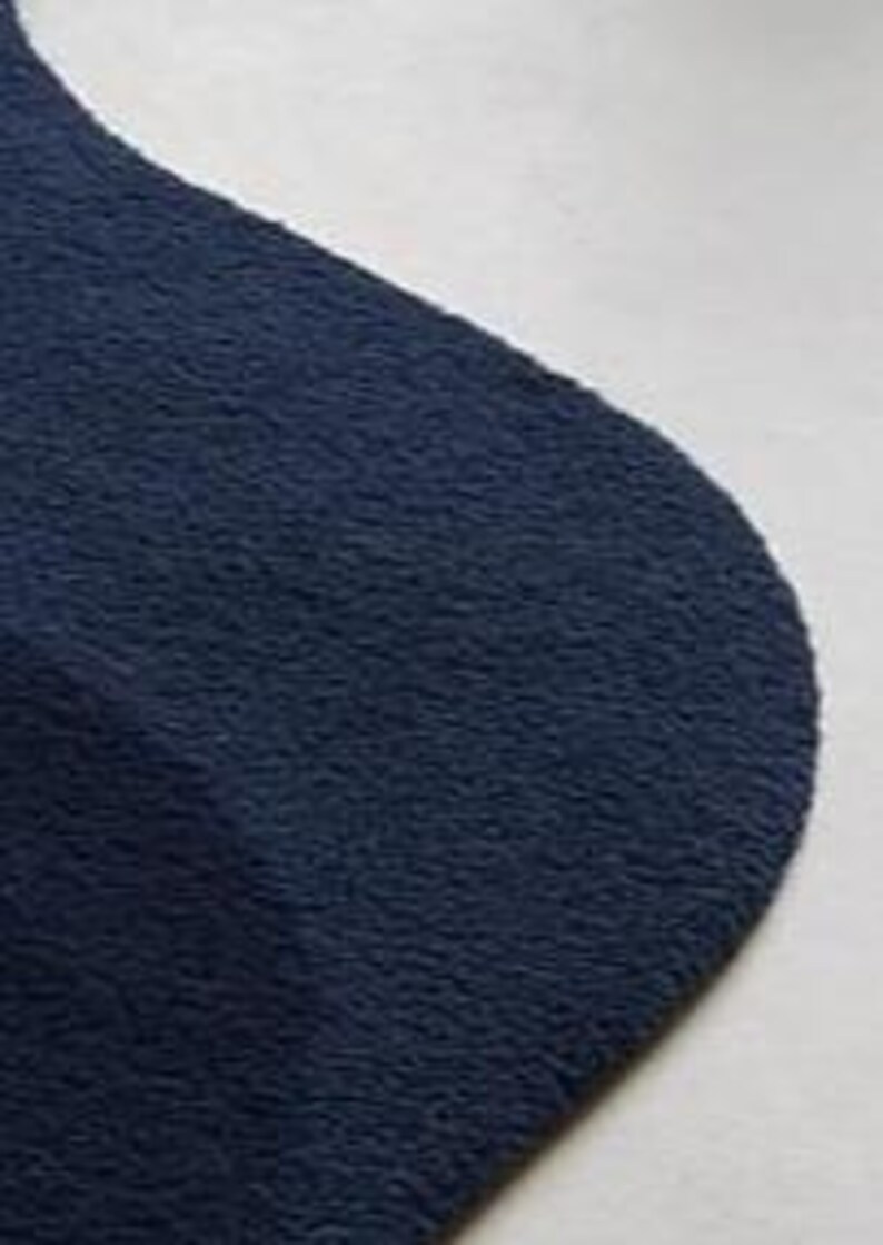Puede incluir: Primer plano de un calcet&iacute;n azul marino con un aspecto suave y texturizado. El calcet&iacute;n est&aacute; hecho de un material afelpado y tiene una punta redondeada. El fondo es de color claro y neutro.