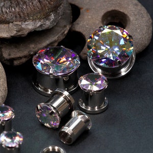 Può includere: Un set di dilatatori per orecchie con gemme iridescenti in varie dimensioni. I dilatatori sono realizzati in acciaio inossidabile e presentano una varietà di dimensioni e stili.