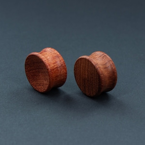 May include: Two brown wooden ear gauges, one on the left and one on the right, on a dark grey background.