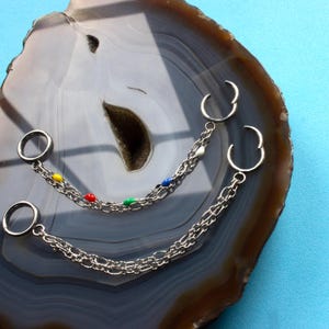 May include: Two silver-toned metal chain connectors, each featuring two circular rings joined by a double-link chain. One chain is accented with small, colourful enamel beads in yellow, red, blue, and green, while the other is plain silver.