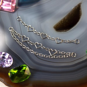 May include: Two silver-toned metal jewellery connectors featuring delicate chain links and open heart-shaped charms. The top connector has three heart charms, while the bottom connector features a double-chain design with three heart charms.