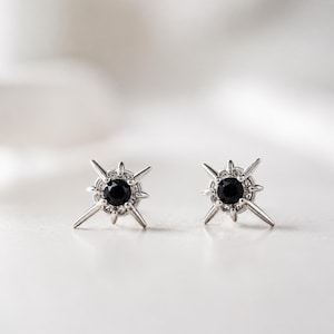Puede incluir: Un par de pendientes de bot&oacute;n de plata con una piedra negra redonda central rodeada por un dise&ntilde;o de estrella con m&uacute;ltiples puntas radiantes. El engaste de metal es de plata pulida y los pendientes tienen una forma de estrella sim&eacute;trica.