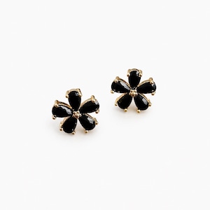 May include: A pair of stud earrings featuring a flower design with five black pear-shaped stones arranged around a central point. The stones are set in a gold-toned metal frame, creating a distinct floral silhouette for each individual earring.