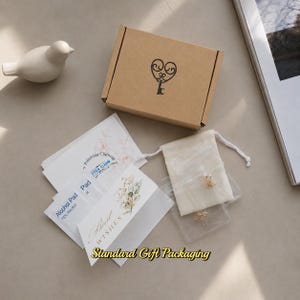 Puede incluir: Una caja de regalo de cart&oacute;n marr&oacute;n con un logotipo de llave en forma de coraz&oacute;n negro, una peque&ntilde;a bolsa de cord&oacute;n color crema con joyas, dos toallitas de alcohol blancas, un pa&ntilde;o de pulido y una tarjeta blanca con motivos florales.