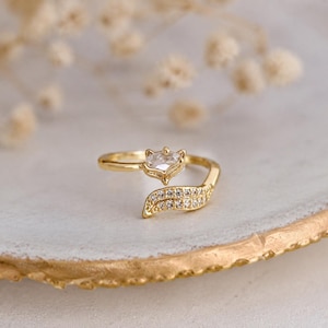 May include: A gold-toned open ring featuring a fox head design at one end with a clear stone and a curved tail at the other end encrusted with small clear crystals. The band is thin and polished, showcasing a delicate animal-inspired motif.