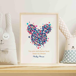 Puede incluir: Una impresión enmarcada en blanco con una silueta de Mickey Mouse de colores hecha de corazones. El texto debajo dice "You are and always have been my dream. Mickey Mouse."
