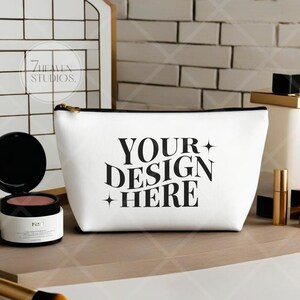 May include: White zippered makeup bag with black text that reads "YOUR DESIGN HERE" and two small stars on either side of the text.
