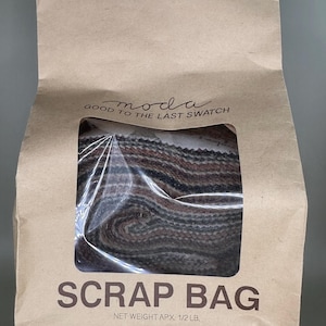 May include: A brown paper bag labelled "SCRAP BAG" with a clear window showing fabric scraps. The bag has the text "moda good to the last swatch" printed above the window. The net weight is approximately 227 grams.