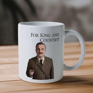 May include: White ceramic mug with a cartoon illustration of a man in a military uniform. The text "For King and Country!" is printed on the mug.