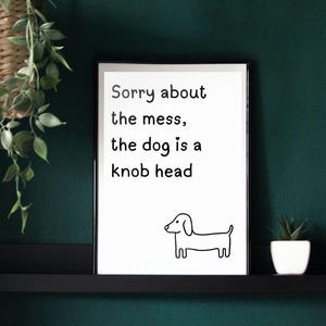 Puede incluir: Una impresión enmarcada blanca con texto negro que dice "Lo siento por el desorden, el perro es un cabezota". Un simple dibujo de línea negra de un dachshund está en la parte inferior de la impresión.
