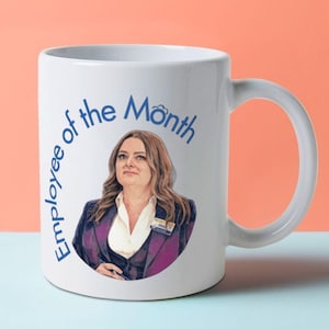May include: White ceramic coffee mug with a blue and white design. The mug features a woman with brown hair and a name tag that says "Chris". The text "Employee of the Month" is written in a blue circle around the woman's image.