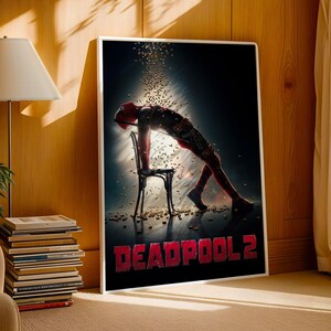 May include: A framed poster featuring the Deadpool 2 movie. The poster shows a figure in a red and black suit leaning over a chair, with the title "DEADPOOL 2" in red at the bottom. The background is dark with golden particles.