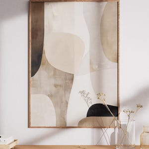 Op de afbeelding: Abstracte kunstprint in een houten lijst. Het kunstwerk toont organische vormen in tinten beige, bruin en zwart. De print wordt tentoongesteld op een houten oppervlak met een vaas met gedroogde bloemen.
