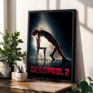May include: A framed poster featuring the Deadpool 2 movie. The poster shows Deadpool leaning over a chair with a shower of gold confetti. The title "DEADPOOL 2" is in red block letters at the bottom.