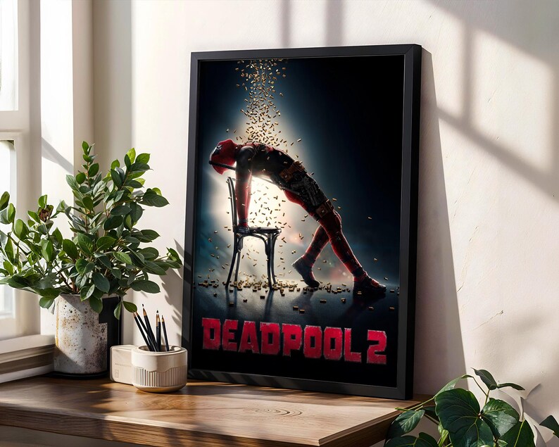 May include: A framed poster featuring the Deadpool 2 movie. The poster shows Deadpool leaning over a chair with a shower of gold confetti. The title "DEADPOOL 2" is in red block letters at the bottom.