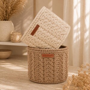 Puede incluir: Dos cestas de almacenamiento cil&iacute;ndricas hechas de cuerda trenzada gruesa. La cesta superior es de color crema y la inferior es de color tostado. Cada cesta tiene una peque&ntilde;a etiqueta rectangular de cuero marr&oacute;n con la palabra Handmade grabada.