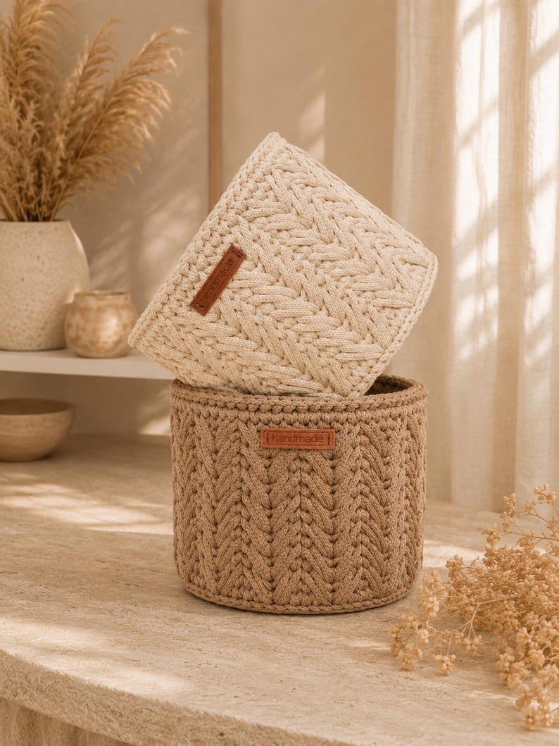 Puede incluir: Dos cestas de almacenamiento cil&iacute;ndricas hechas de cuerda trenzada gruesa. La cesta superior es de color crema y la inferior es de color tostado. Cada cesta tiene una peque&ntilde;a etiqueta rectangular de cuero marr&oacute;n con la palabra Handmade grabada.