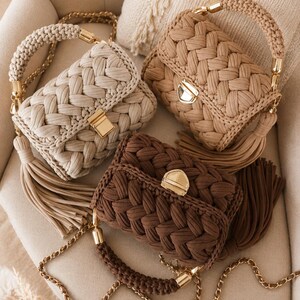 May include: Three rectangular handbags featuring a thick braided fabric texture in cream, beige, and dark brown. Each bag includes a gold-tone metal clasp, a matching braided top handle with gold hardware, a long chain shoulder strap, and a side tassel.
