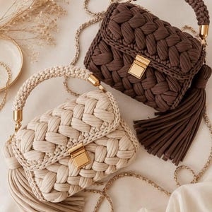 May include: Two handbags crafted from thick, braided fabric cord. One bag is dark brown and the other is cream. Both feature a gold-tone metal rectangular clasp, a matching braided top handle with gold hardware, and a long, thin gold chain strap.