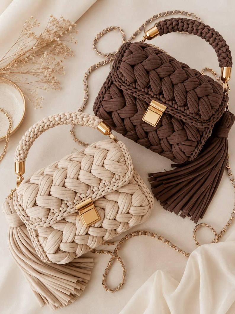 May include: Two handbags crafted from thick, braided fabric cord. One bag is dark brown and the other is cream. Both feature a gold-tone metal rectangular clasp, a matching braided top handle with gold hardware, and a long, thin gold chain strap.