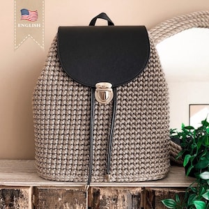May include: A beige crocheted backpack with a black faux leather flap and a gold metal buckle closure. The backpack has a drawstring closure and a long black strap.