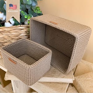 Puede incluir: Dos cestas de almacenamiento de crochet beige con asas de cuero. Las cestas están apiladas una encima de la otra.