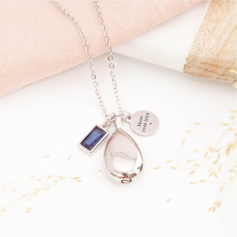Silver cremation teardrop necklace with September birthstone and personalised engraving tag on display
