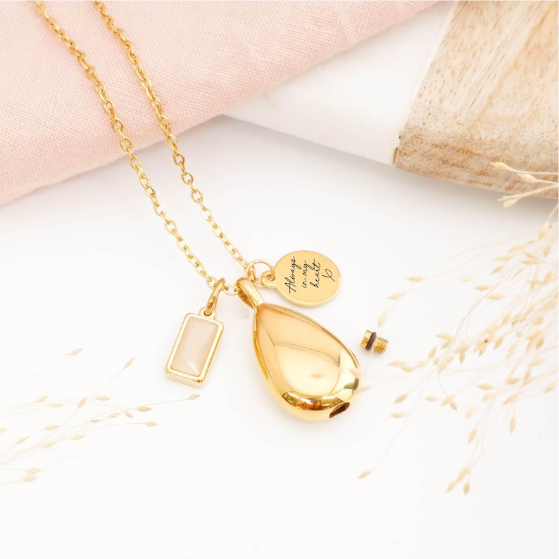Gold ashes teardrop necklace with June birthstone and engraved tag, laid on wooden table