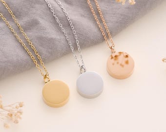 May include: Three silver necklaces with round pendants. The pendants are gold, silver, and rose gold. The necklaces are on a grey fabric background.