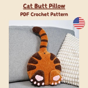 May include: A plush, orange and brown cat butt pillow with a striped tail and pink paw pads. The text "Cat Butt Pillow PDF Crochet Pattern" is displayed above the pillow. The words "Sewing required" are at the bottom.