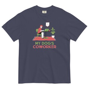 May include: A navy blue t-shirt featuring a graphic of a person working at a desk with a laptop. The text "MY DOG'S COWORKER" is printed below the graphic.