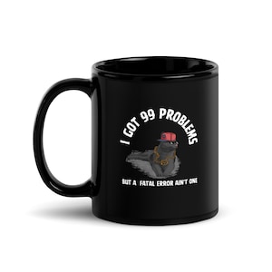 Puede incluir: Taza de café de cerámica negra con un gráfico blanco de un gato negro con una gorra de béisbol roja y una cadena dorada. El texto dice "Tengo 99 problemas pero un error fatal no es uno".