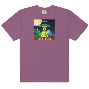 Puede incluir: Camiseta morada con un gráfico pixelado de un OVNI sobrevolando una montaña con el texto "GIT PULL" debajo.