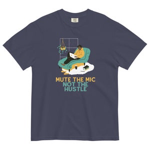 May include: A navy blue t-shirt featuring a graphic of a person sitting in a chair with a laptop, a book, and a cup of coffee. The text "Mute the mic not the hustle" is printed below the graphic.