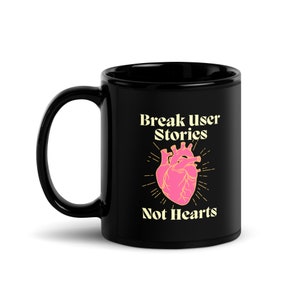 以下が含まれることがあります： ピンクのハートと「Break User Stories Not Hearts」という黄色のテキストが書かれた黒いセラミック製のコーヒーカップです。