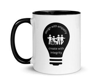 May include: White ceramic mug with a black rim and handle. The mug features a black and white illustration of a light bulb with the text "design with empathy create with integrity" and a graphic of four people, one in a wheelchair, standing together.