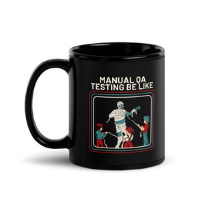 Può includere: Tazza da caffè nera con una grafica bianca di una mummia tirata da tre bambini. Il testo "MANUAL QA TESTING BE LIKE" è sopra la grafica.