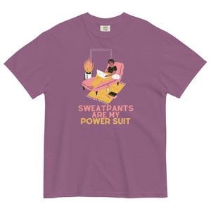 May include: Mauve t-shirt with the text "Sweatpants are my Power Suit." The graphic shows a person relaxing on a pink chaise lounge with a laptop, a rug, and a potted plant. The shirt is a Comfort Colors brand.