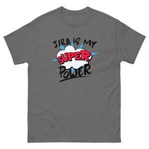 以下が含まれることがあります： 「JIRA IS MY SUPER POWER」という文字がコミック風に描かれたグレーのTシャツ。 文字は白、赤、黒で、背後には青いスターバーストのデザインがあります。