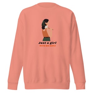 Op de afbeelding: Koraalrood sweatshirt met een afbeelding van een persoon die bloemen vasthoudt, met de tekst "Just a girl with big data." De persoon draagt een oranje top en een groene broek. De sweatshirt heeft lange mouwen en een ronde hals.