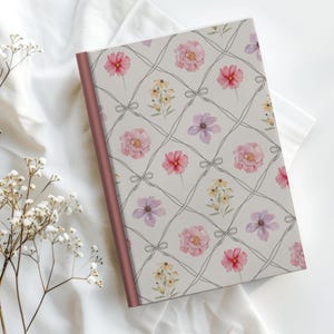 Puede incluir: Un diario floral con un fondo gris claro, con un patr&oacute;n de cuadr&iacute;cula con flores rosas, rojas, amarillas y moradas. El diario tiene una columna vertebral de color rosa y un fondo blanco.
