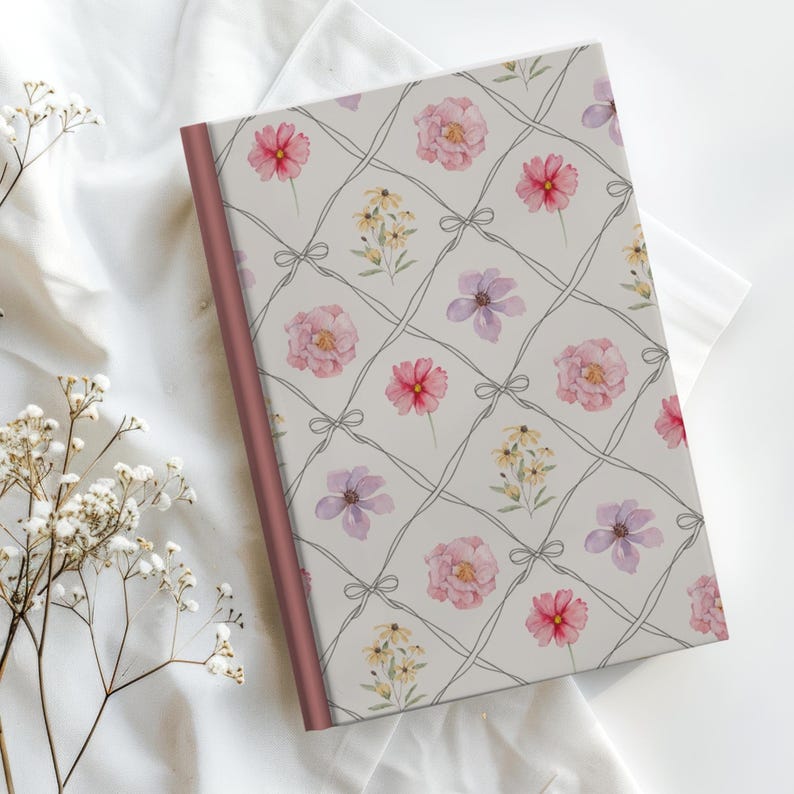 Puede incluir: Un diario floral con un fondo gris claro, con un patr&oacute;n de cuadr&iacute;cula con flores rosas, rojas, amarillas y moradas. El diario tiene una columna vertebral de color rosa y un fondo blanco.