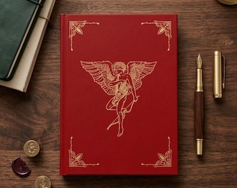 May include: A red hardcover journal featuring a gold-foiled illustration of a winged figure with a blindfold, bow, and arrow. The cover includes ornate gold corner accents. Beside the journal are a wooden fountain pen, a metal cap, and wax seals.