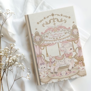 May include: A rectangular notebook with a cream-colored cover featuring a carousel illustration. The design includes a white lamb, a small cat, and a teddy bear, with the text "Small Creatures Theme Park" printed in a decorative script font.