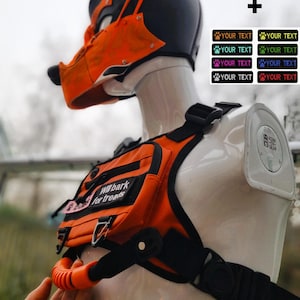 以下が含まれることがあります： 黒とオレンジ色のパップフードとハーネスセット。フードはオレンジ色のアクセントと犬のような鼻が特徴です。ハーネスには「Will bark for treats」の文字が入ったポーチが付いています。「YOUR TEXT」の文字が入ったカスタマイズ可能な足跡ステッカーが含まれています。