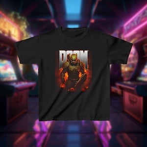 May include: Black t-shirt featuring the word "DOOM" in white block letters above a detailed graphic of a character in green armor, set against a fiery background. The design includes skulls and a weapon, evoking a video game theme.