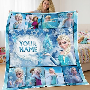 Könnte beinhalten: Eine blau-weiße Decke mit Bildern einer Zeichentrickfigur mit blonden Haaren und dem Text "YOUR NAME". Die Decke hat ein Schneeflocken- und Eisburg-Design. Die Decke wird von einer Person gehalten.