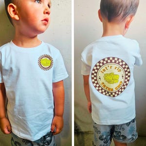 May include: A light blue t-shirt with a circular graphic on the front and back. The graphic features a yellow tater chip design inside a brown and white checkered circle. The back of the shirt has the words "let'r rip tater chip".